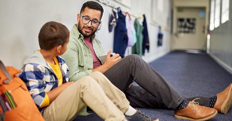 Teacher and student sitting in the hallway chatting.
